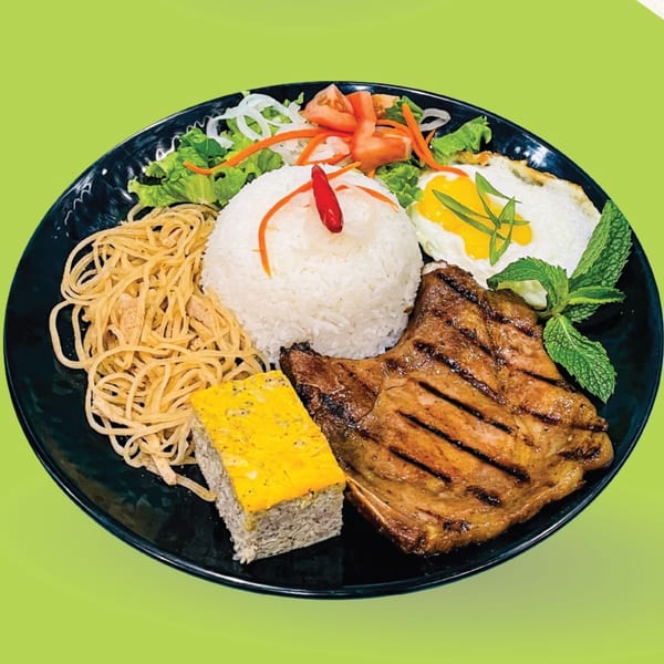 Vietnamese grilled pork chop with rice, fried egg, shredded pork skin, and vegetables on a black plate.