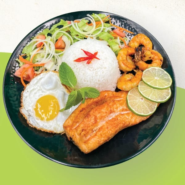 Grilled salmon, shrimp, fried egg, rice, and salad with lime slices on a black plate.